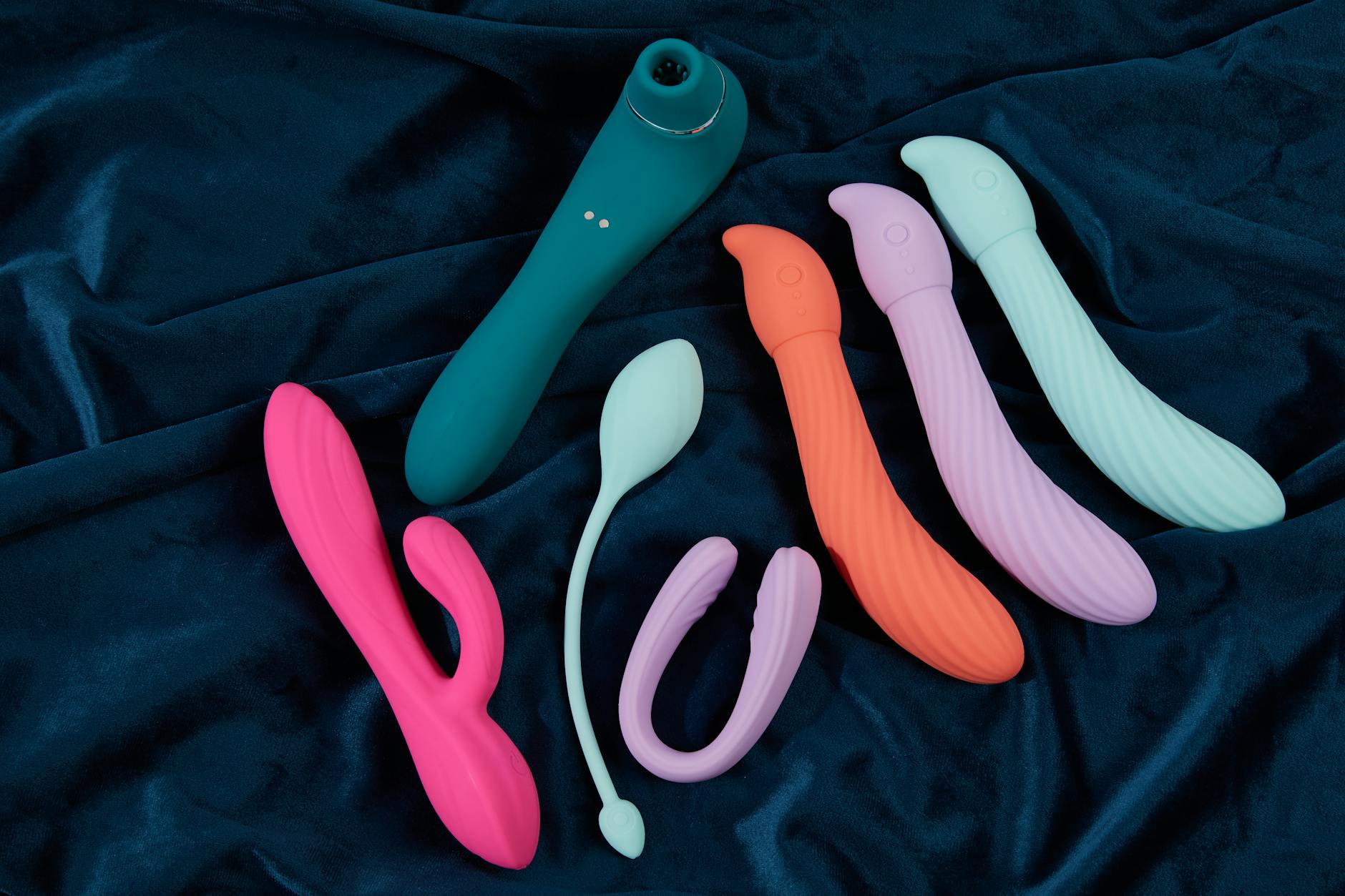 Una collezione di vibratori colorati su tessuto di seta blu, che mostra diverse forme e texture.