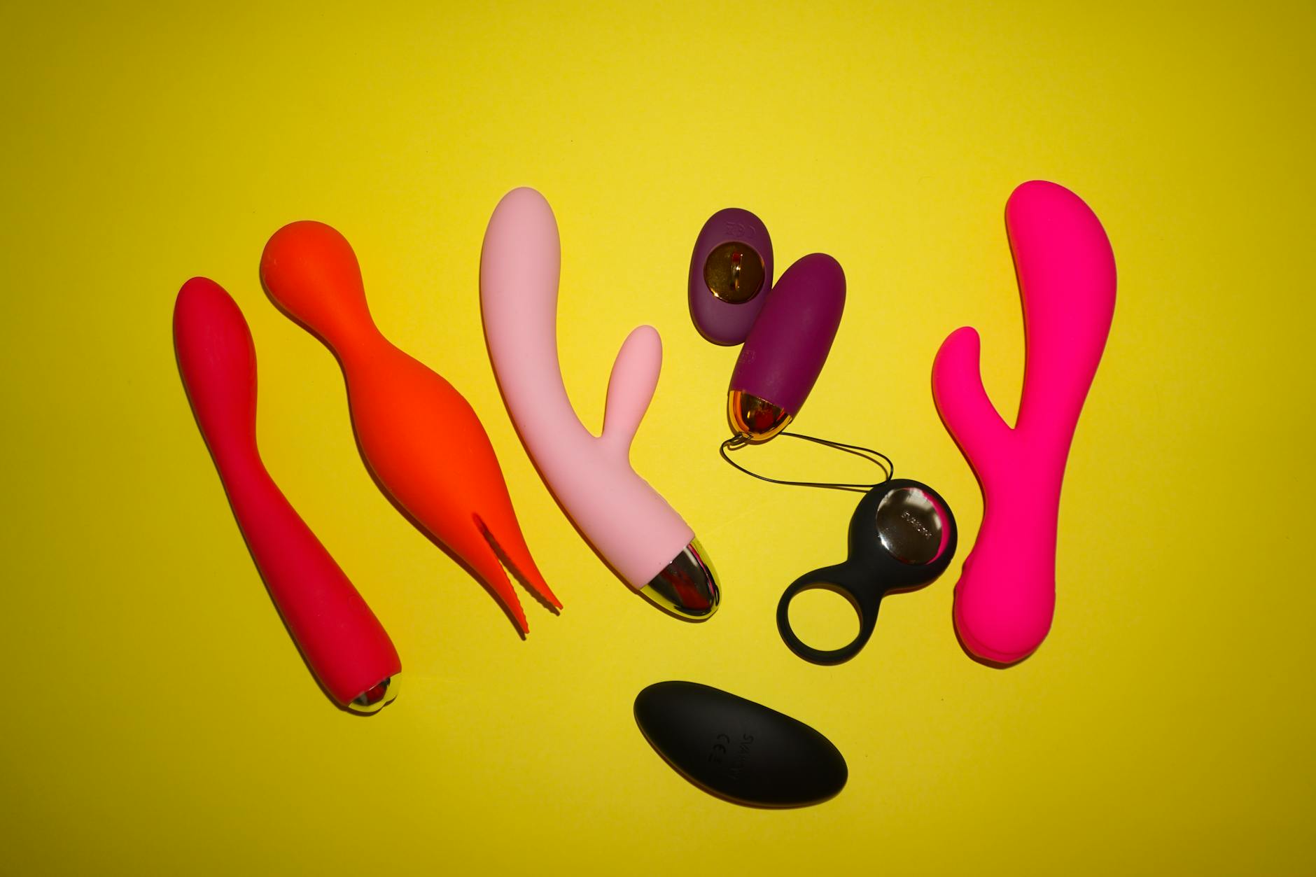 Colorful clitoral vibrators and toys arranged on a bright yellow background